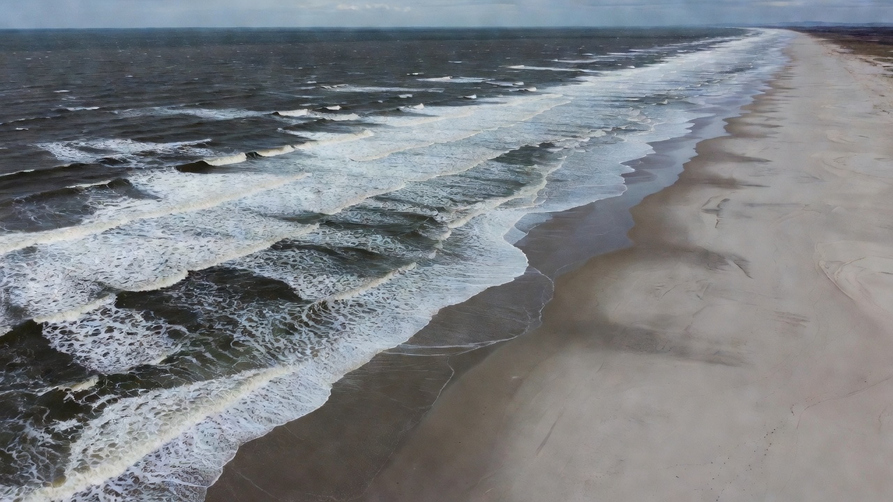 Aerial view of waves meeting a long sandy northern European coastline