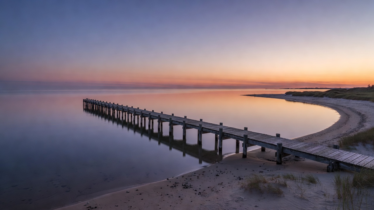 Jetty extending over calm coastal water beside a quiet shoreline at dusk